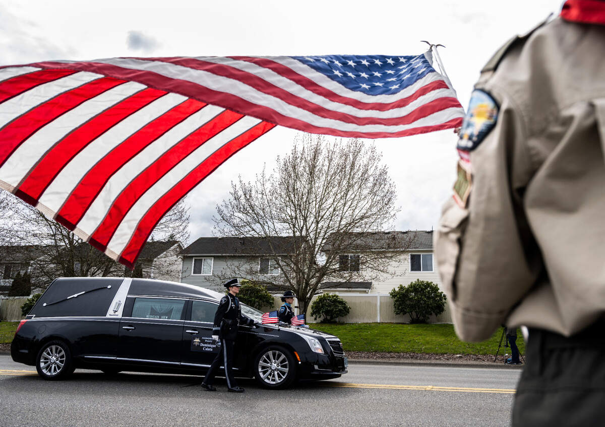 Boy Scout Thomas Faria, 10, with Troop DXVI holds an American flag in honor of deputy Dom Calata as Calata’s hearse passes by during the procession to his celebration of life at the Church for All Nations in Tacoma on Friday, March 25, 2022. Calata was killed in the line of duty during a SWAT operation on March 15, 2022.