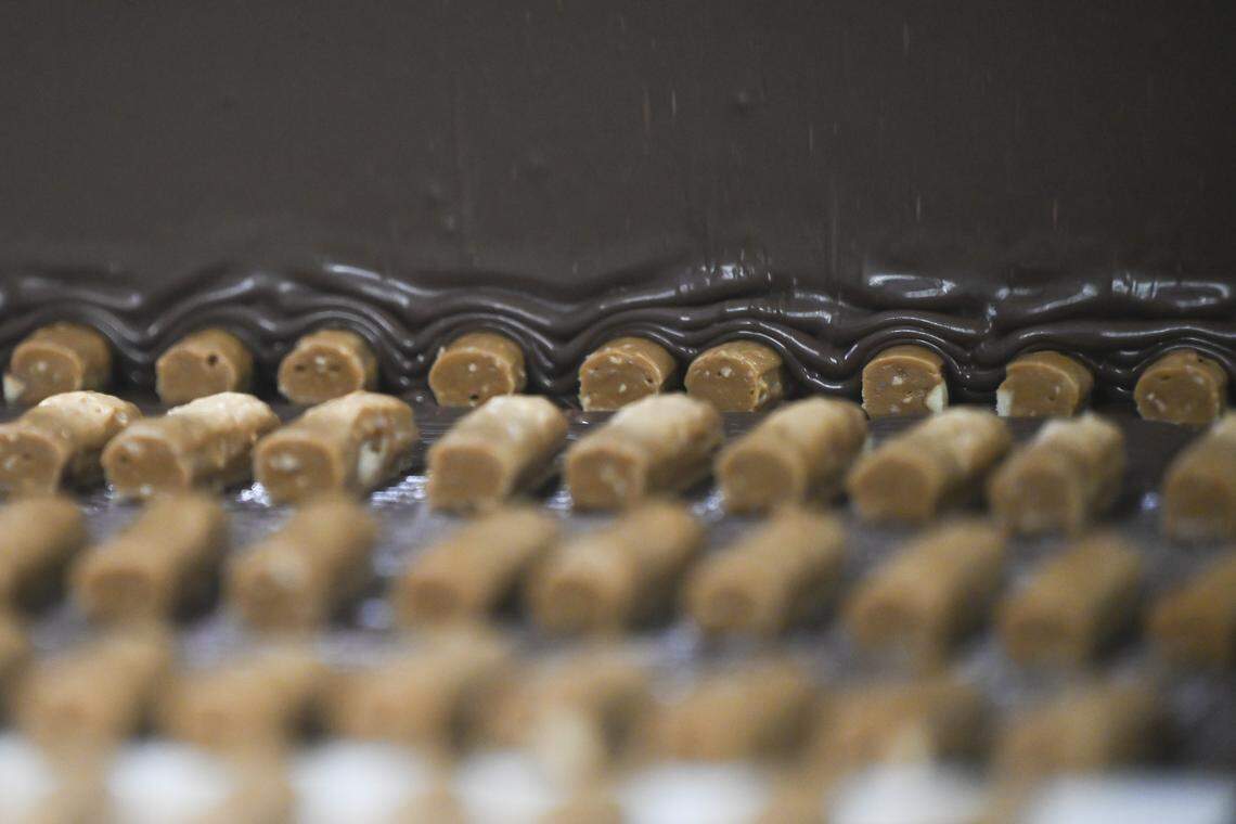 A curtain of chocolate covers cut toffee as the candies moves along a conveyor belt on Tuesday, April 7, 2026, at the Brown & Haley factory in Tacoma.