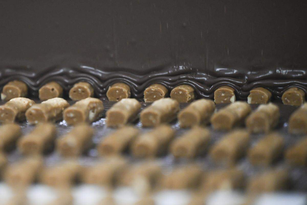 A curtain of chocolate covers cut toffee as the candies moves along a conveyor belt on Tuesday, April 7, 2026, at the Brown & Haley factory in Tacoma, Wash.