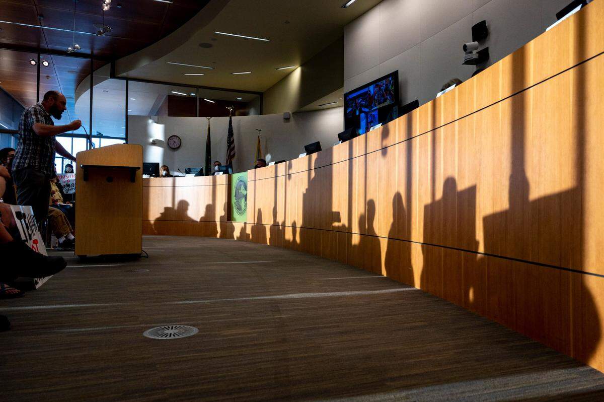 Ty Moore, an organizer with Home in Tacoma For All, addresses the Puyallup City Council as the shadows of several people holding signs are seen in front of him during a meeting on Tuesday, Aug. 23, 2022.