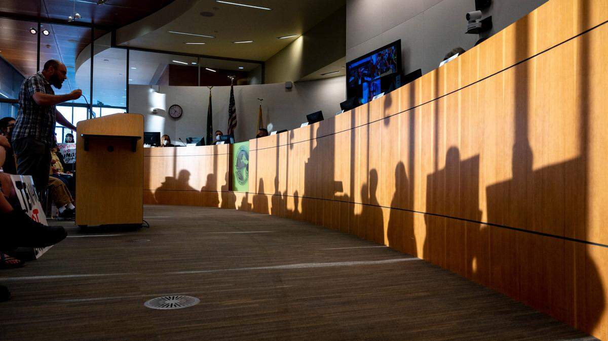 Tyron Moore, an organizer with Tacoma For All, addresses the Puyallup City Council as the shadows of several people holding signs are seen in front of him during a meeting on Tuesday, Aug. 23, 2022.