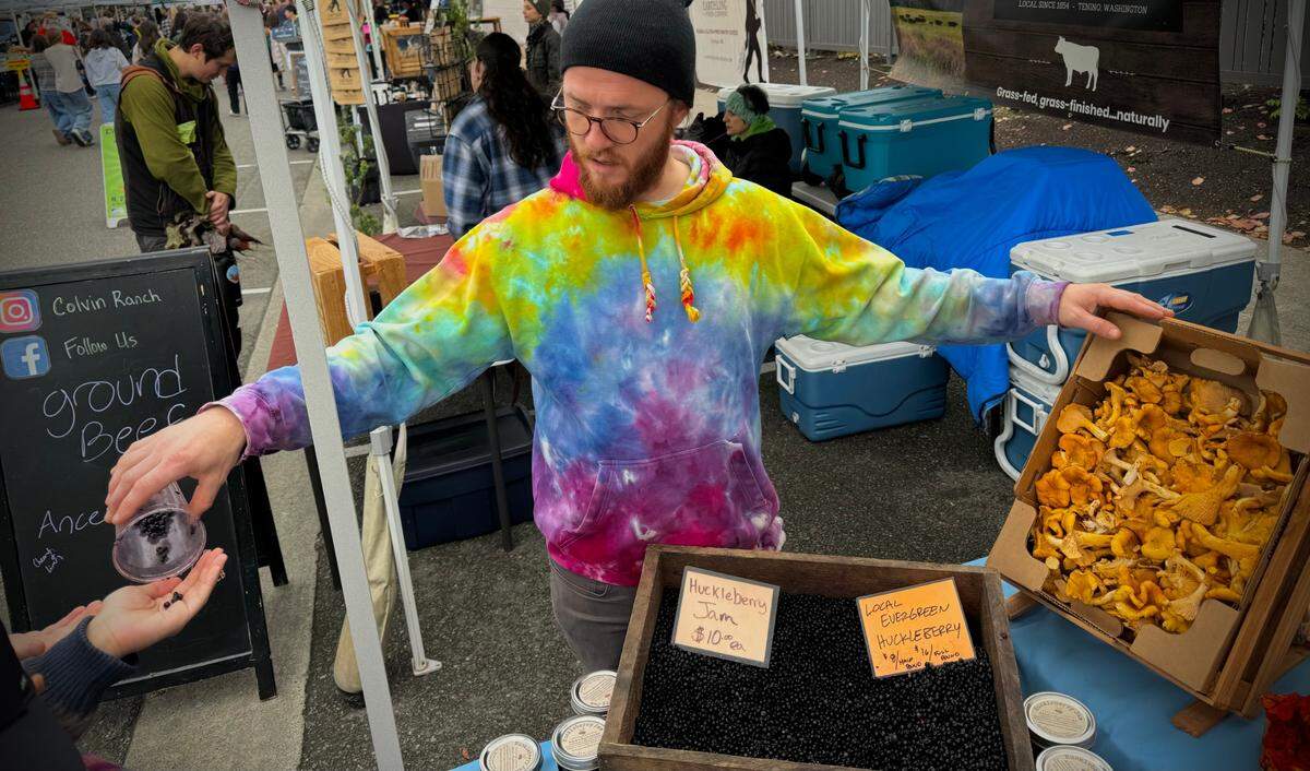 Tim Hartman, operations manager for Adam’s Mushrooms, hands a huckleberry sample to Henry Hua at Tacoma’s Proctor Farmers Market on Saturday, Oct. 19, 2024.