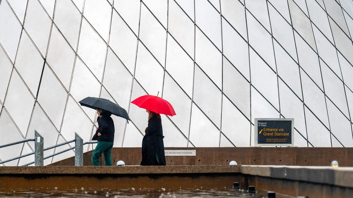 A pair of umbrella-clad women walk past the Museum of Glass in downtown Tacoma on a rainy Monday afternoon.