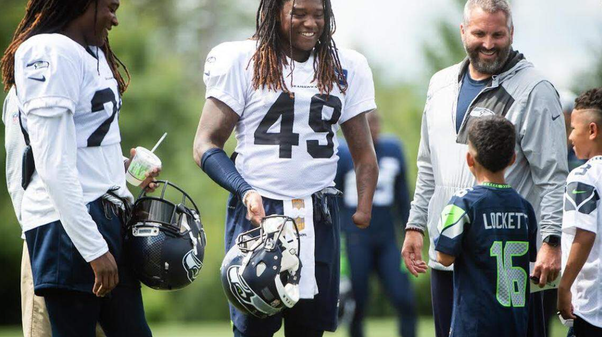 Shaquill Shaquill Griffin (26), twin brother and then-Seahawks teammate Shaquem Griffin (49) and Seahawks Vice President for Communications Dave Pearson talk with a young fan following practice at NFL training camp the Virginia Mason Athletic Center in Renton in August 2018. The twins played together on the starting defense for the first time during that NFL training camp.