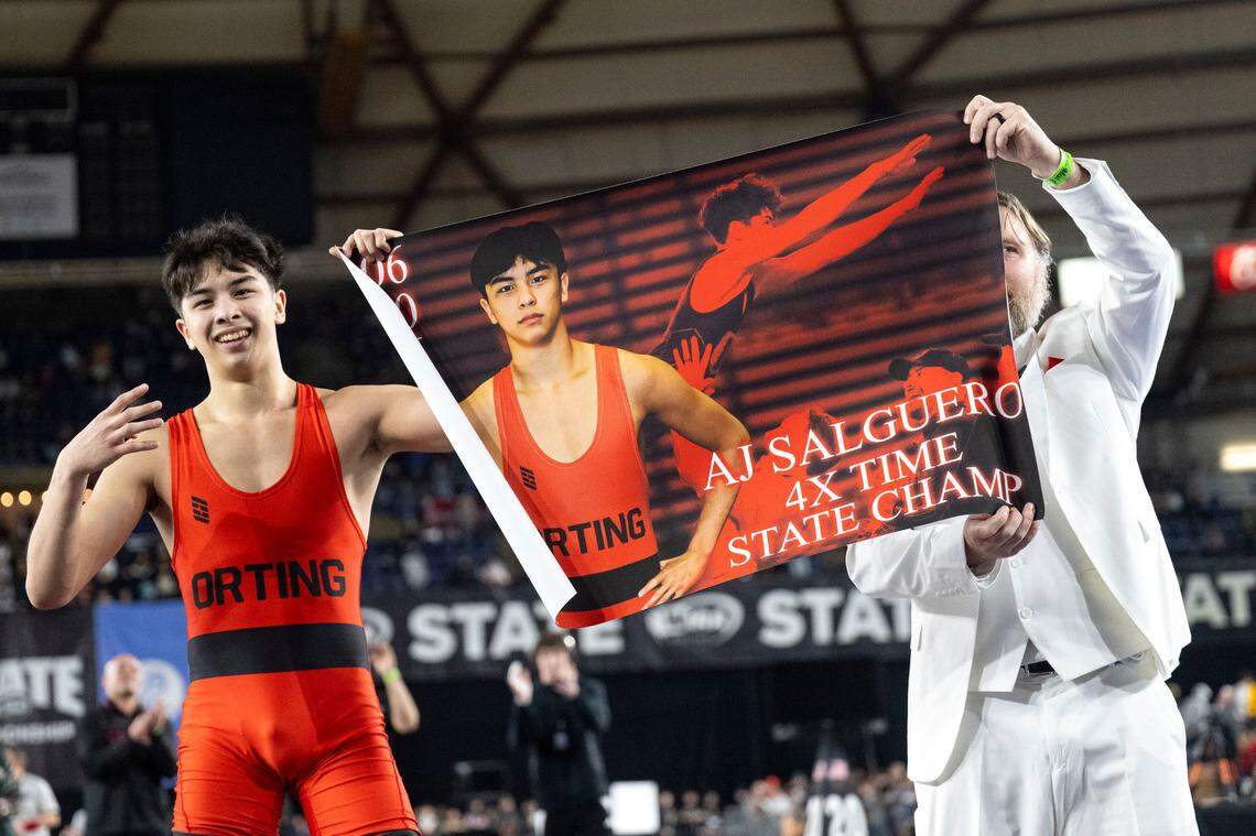 Orting’s Alan Salguero, Jr. and head coach Jody Coleman hold up a poster celebrating Salguero’s fourth-straight state title after he defeated Deer Park’s Gavin Carnahan to win the Class 2A, 138-pound championship match on Saturday, Feb. 22, 2025, at Mat Classic XXXVI at the Tacoma Dome in Tacoma, Wash.