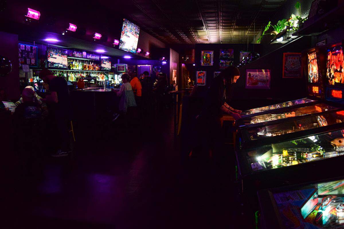 Find pinball and a banquette with table seating to the front. In the bar area, there are high-top tables and a couple TVs.