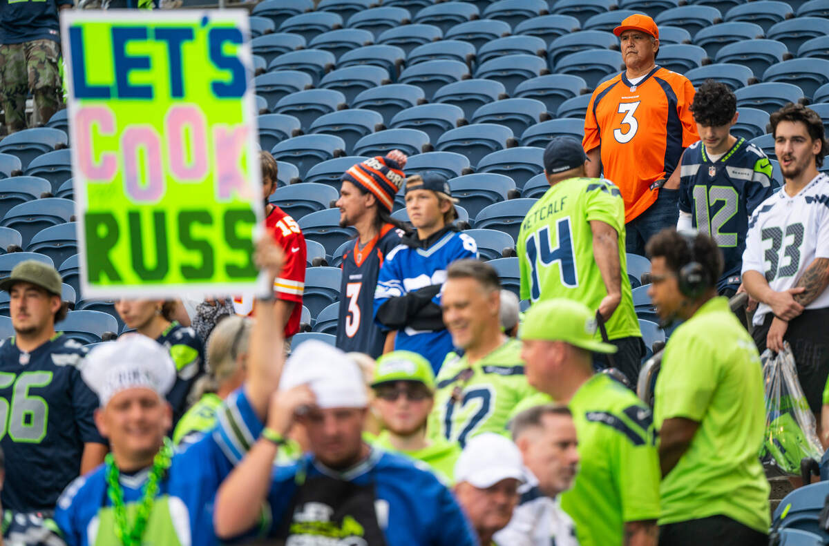 A fan wearing a Russell Wilson jersey stands behind a Seahawks fan holding a sign that reads, “Let’s Cook Russ,” before the start of an NFL game on Monday, Sept. 12, 2022, at Lumen Field in Seattle.