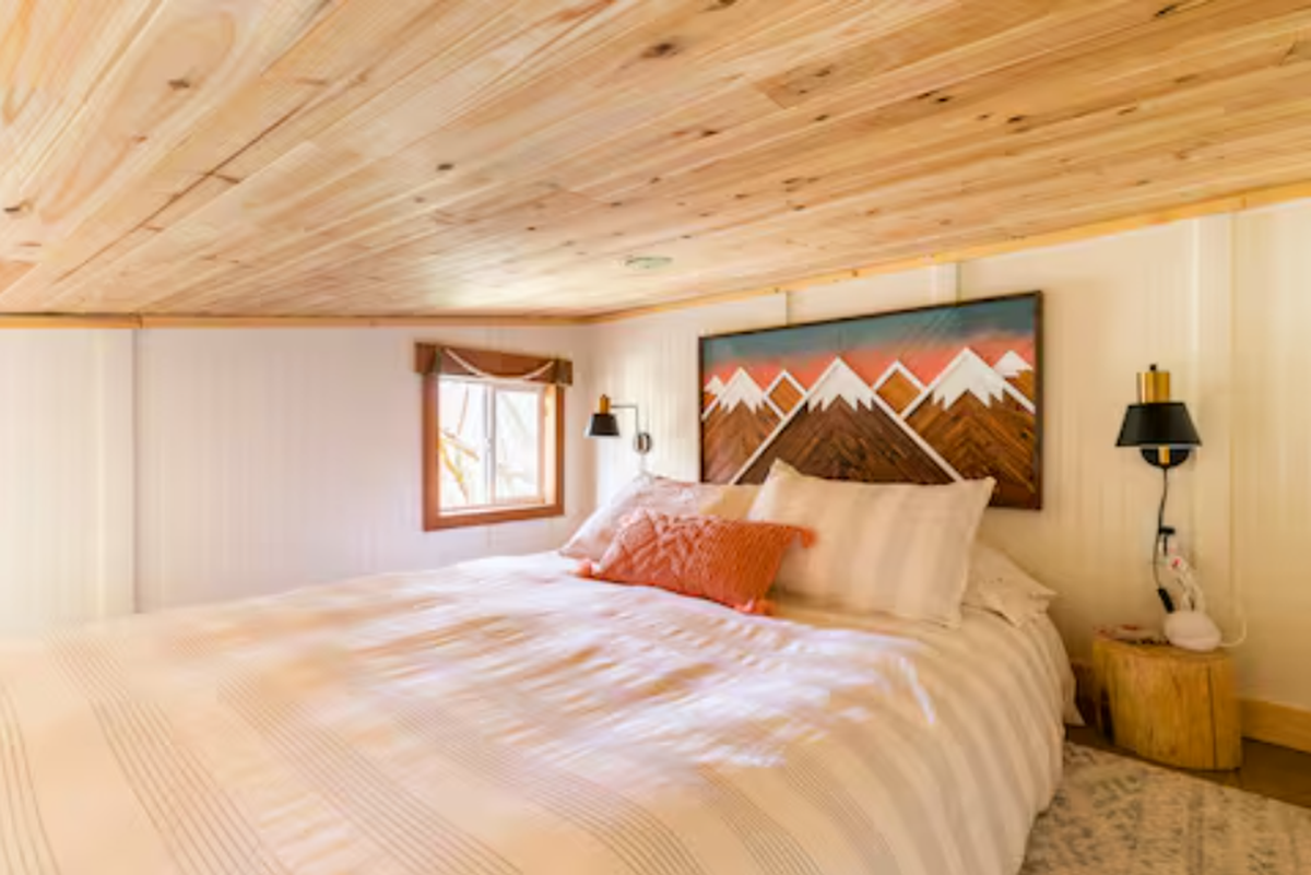 The North Bend treehouse Airbnb hosted by Erica and Tim includes a queen-sized bed on a loft. This photo from the listing has the caption “Cozy loft area with stump side tables and reading sconces, as well as a queen bed complete with plush organic cotton bedding.”
