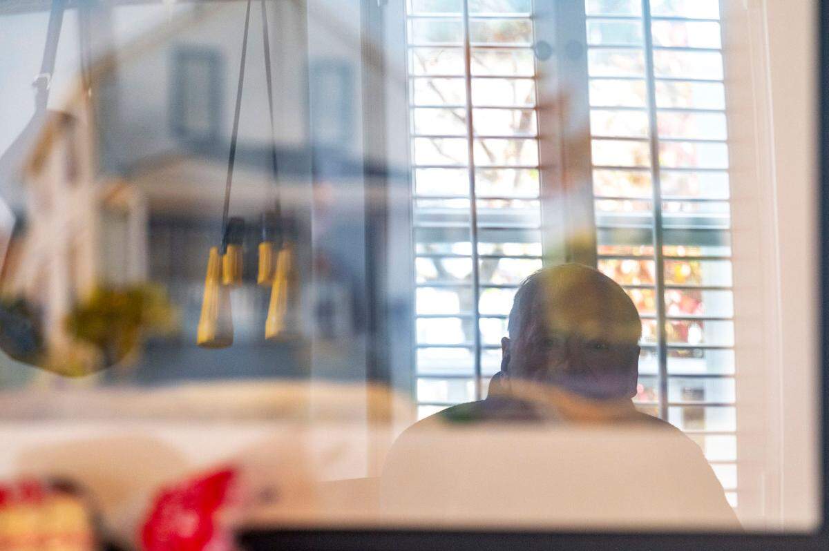 Paul Kadzik is seen in the reflection of a picture of the front of his Gig Harbor home as he sits inside the Airbnb-style rental alongside the second-floor of the house on Thursday, Feb. 24, 2022.