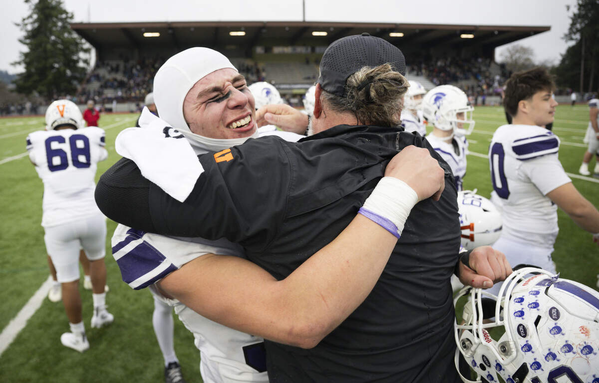 Sumner defensive end Shaun Griffith (90) and Sumner Spartans head coach Keith Ross hug after the Spartans 42-35 victory over Puyallup in the 4A state semifinal game at Sparks Stadium, on Saturday, Nov. 29, 2025 in Puyallup, Wash.