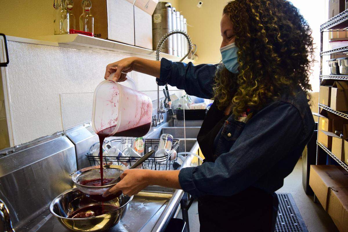 Komadre Kombucha is Tacoma’s first taproom dedicated to the fermented tea, located at 2914 6th Ave. Owner Julie Davidson strains fresh blackberry puree for the Mora Lavender on August 6, 2021.
