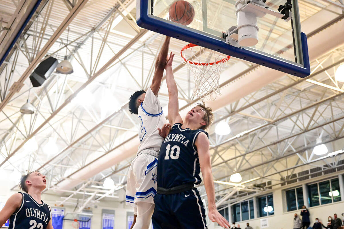 Curtis guard Cinque Maxwell (12) puts in a layup over the outstretched arm of Olympia guard Drew Carlson (10) late in the fourth quarter of a 4A South Puget Sound League game on Friday, Jan. 21, 2022, at Curtis High School in University Place, Wash.