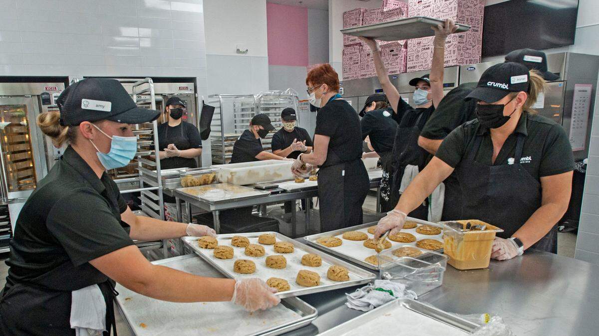 As co-owner Amy Beam, left, and manager Brynan Heim prep a tray of Reese’s peanut butter cookies, a team of employees bustle behind them during the soft launch of the cookie franchise Crumbl at 4784 Borgen Blvd in the Costco complex on Thursday, Oct. 21, 2021.