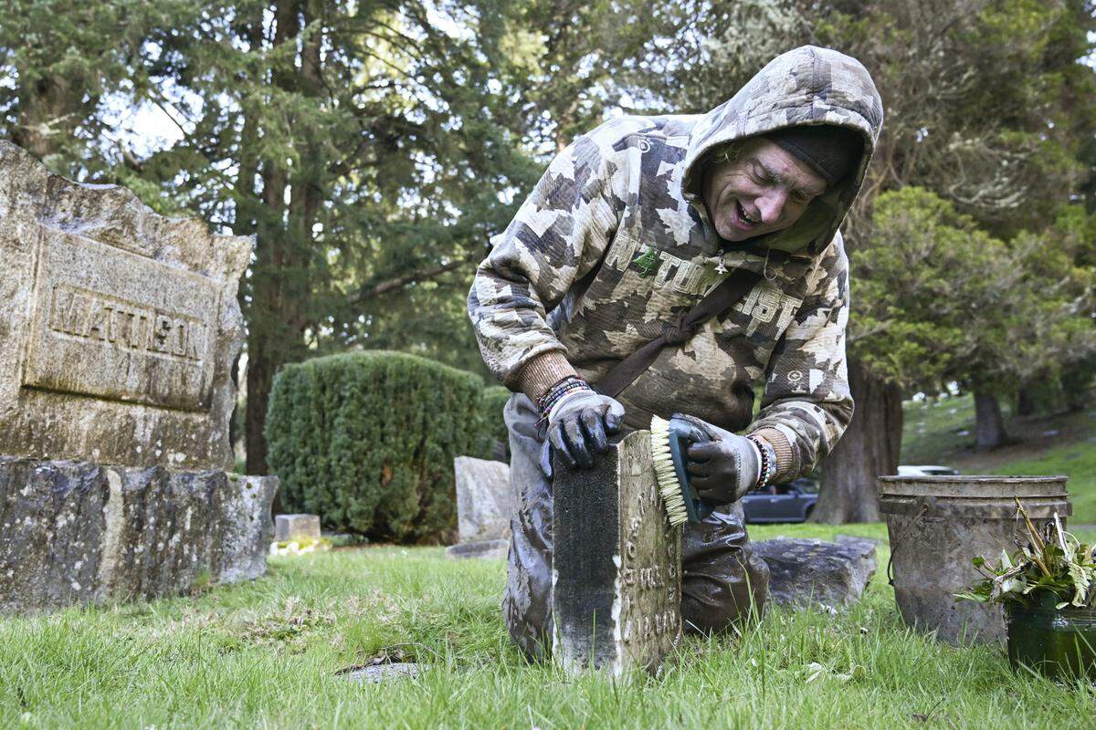 William Fleet kneels to clean a headstone at the old Tacoma Cemetery on Monday, March 9, 2026, in Tacoma, Wash.