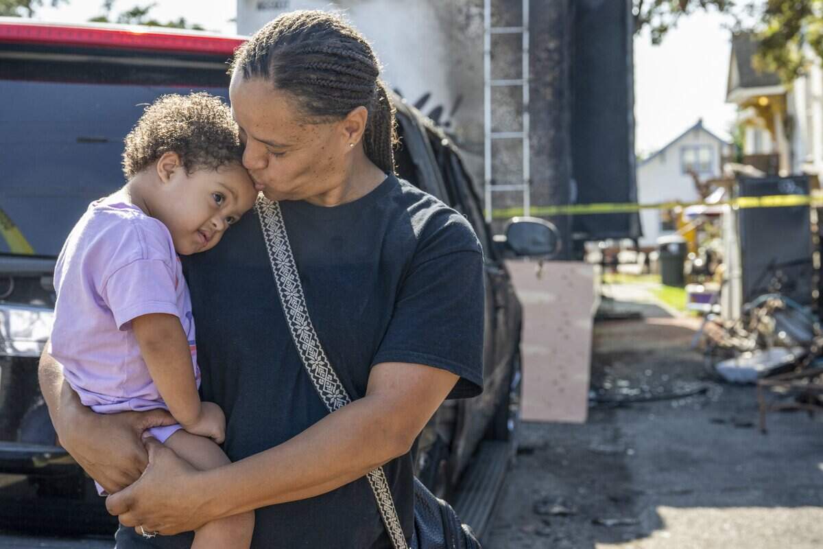 Elliana, 3, is kissed on the forehead by mother Paula Brooks as they look at the fire damage to their house, motorhome and two family cars on Thursday, Sept. 18, 2025, in Tacoma, Wash.