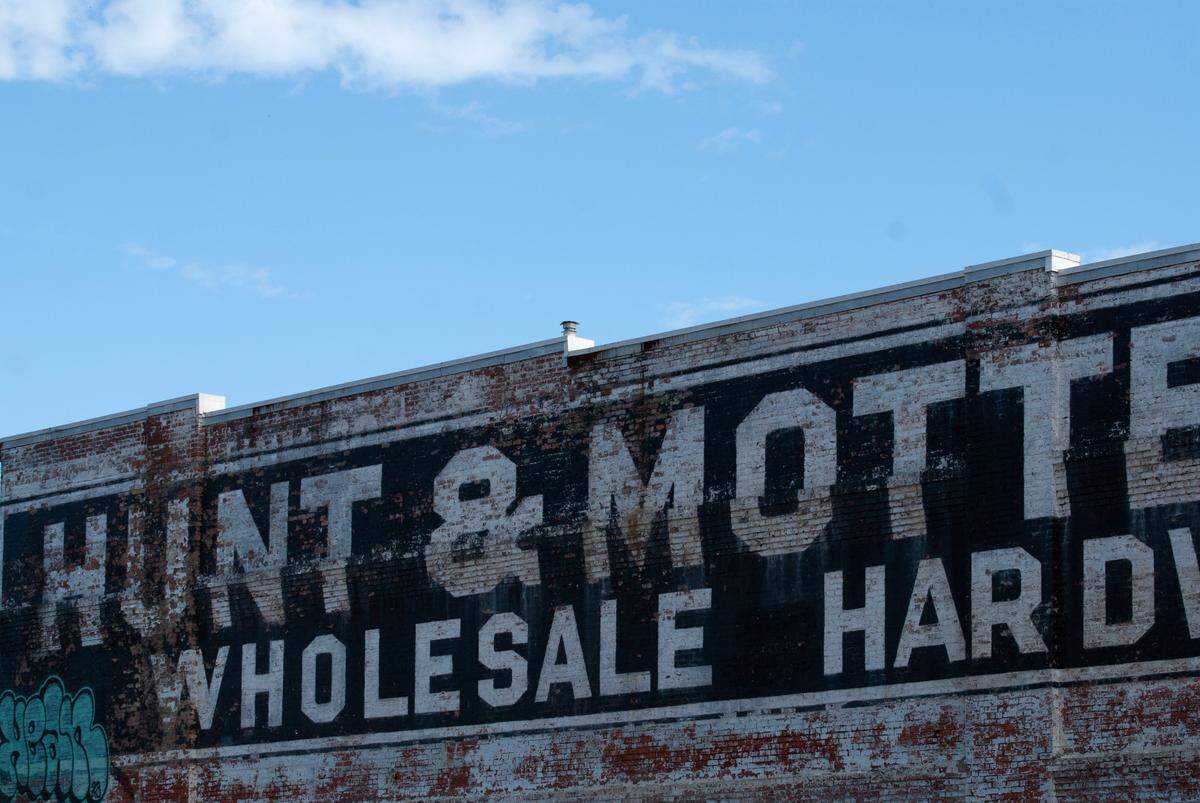 The black-and-white faded Hunt & Mottet wholesale hardware ghost sign contrasting with the bright blue sky in Tacoma. Photographed on July 12, 2023.
