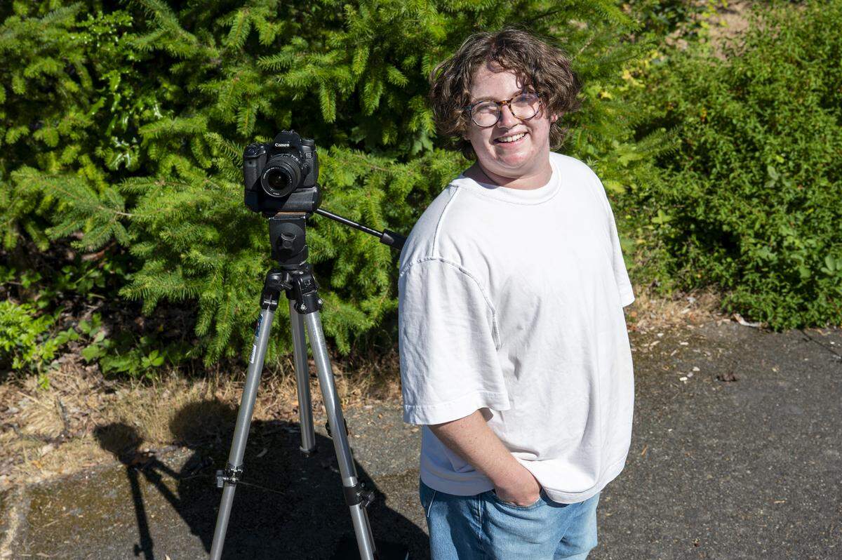 Easton Umansky poses for a photo with his tripod in a neighborhood near Optimist Park on Tuesday, July 15, 2025, in the West End of Tacoma, Wash. Umansky is working on a research project as a student at the University of Puget Sound that includes photographing tree coverage in neighborhoods around Tacoma.