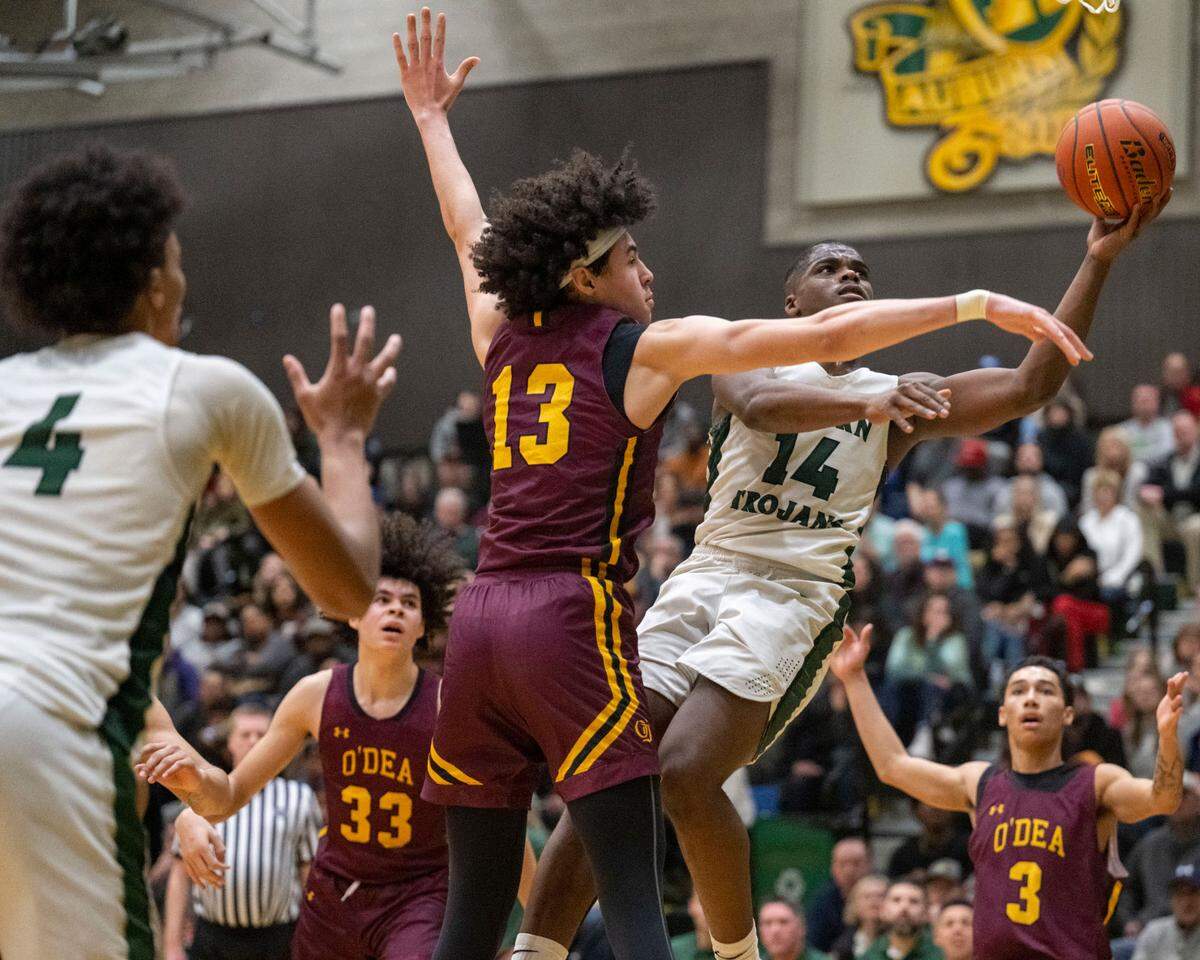Auburn guard Luvens Valcin (14) drives to the basket for a shot attempt as O’Dea forward Miles Clark (13) defends during the third quarter of a Class 3A state regionals game on Saturday, Feb. 25, 2023, at Auburn High School in Auburn, Wash.