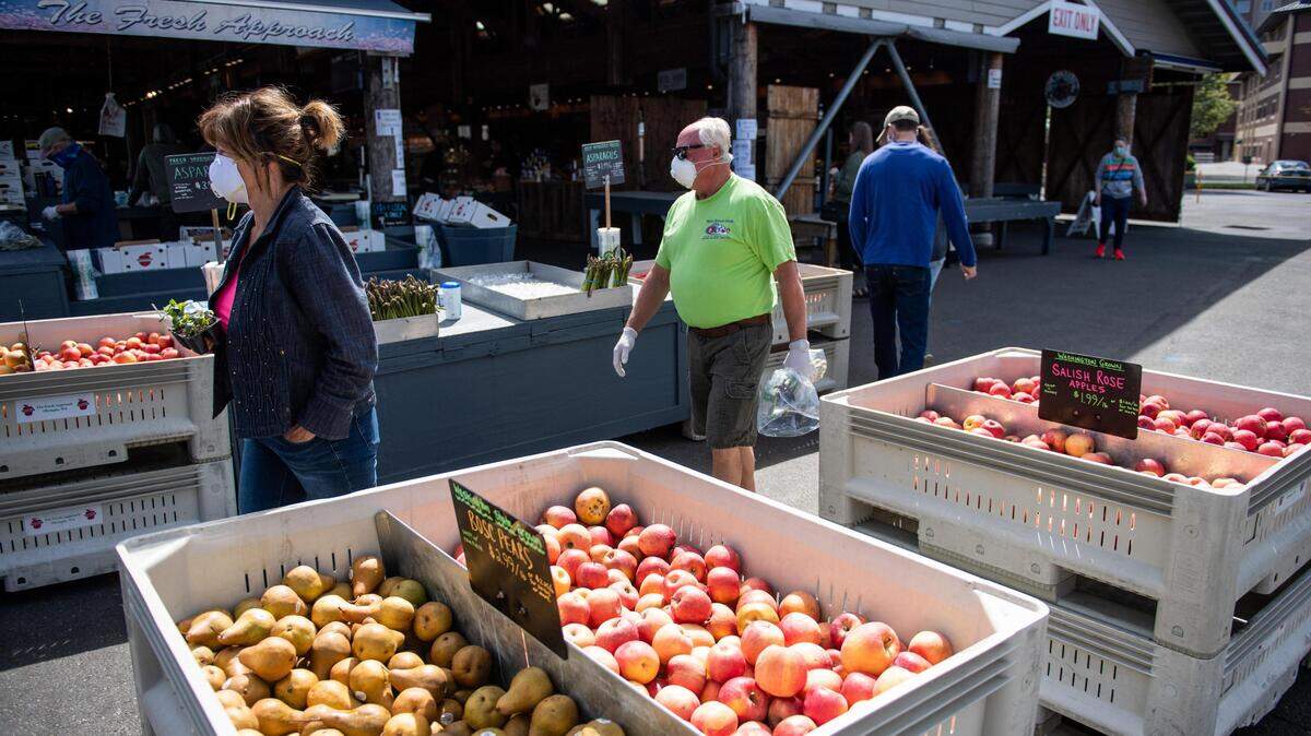 People walk past fruit for sale at the Olympia Farmers Market in Olympia, Wash., on Sunday, April 19, 2020.