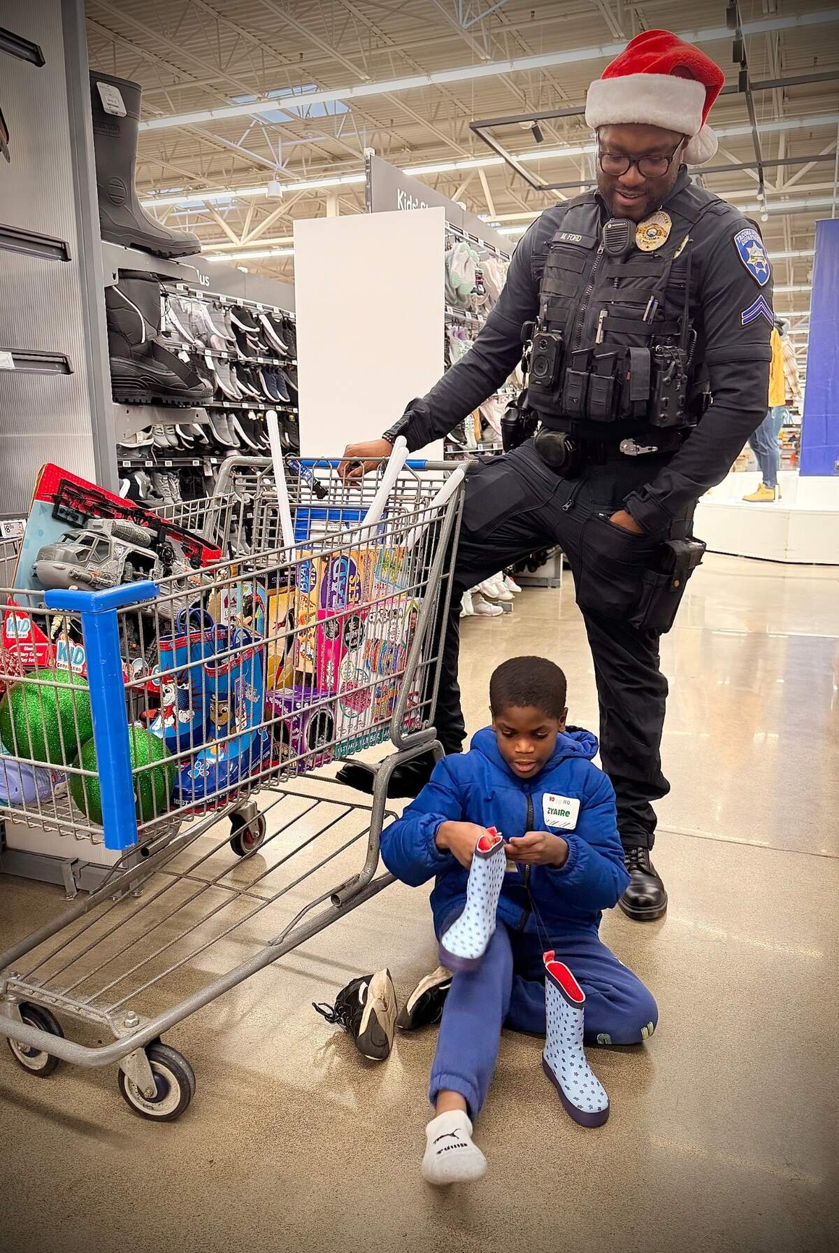 Tacoma Police Specialist Masyih Ford watches Zyaire Coleman, 8, try out a pair of shoes Saturday, Dec. 14, 2024 during the annual Shop With A Tacoma Cop event at Walmart in Tacoma.