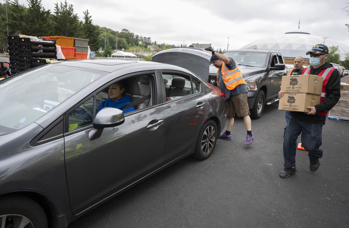 Food is placed in the trunk of Martha Partida’s, left, car during a drive through food distribution with Eloise’s Cooking Pot Food Bank on Wednesday, July 8, 2026, at the Tacoma Dome in Tacoma, Wash.
