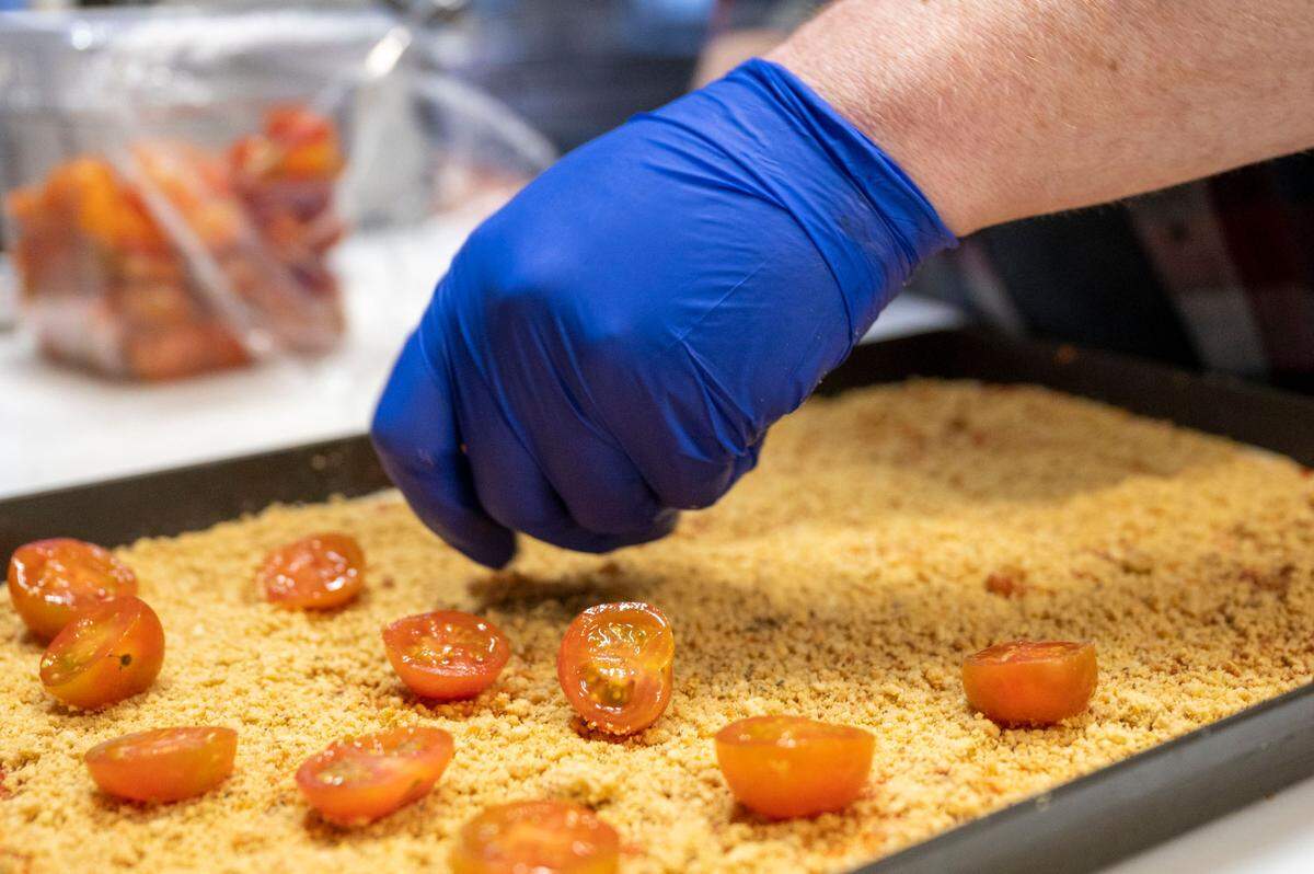 Chef Jacob Thacker adds cherry tomatoes to a layer of housemade vegan parm for The Quickie, one of four bar pies now available at E9 Firehouse. “This pizza is a little more delicate — roasted nuts burn easily,” he said.