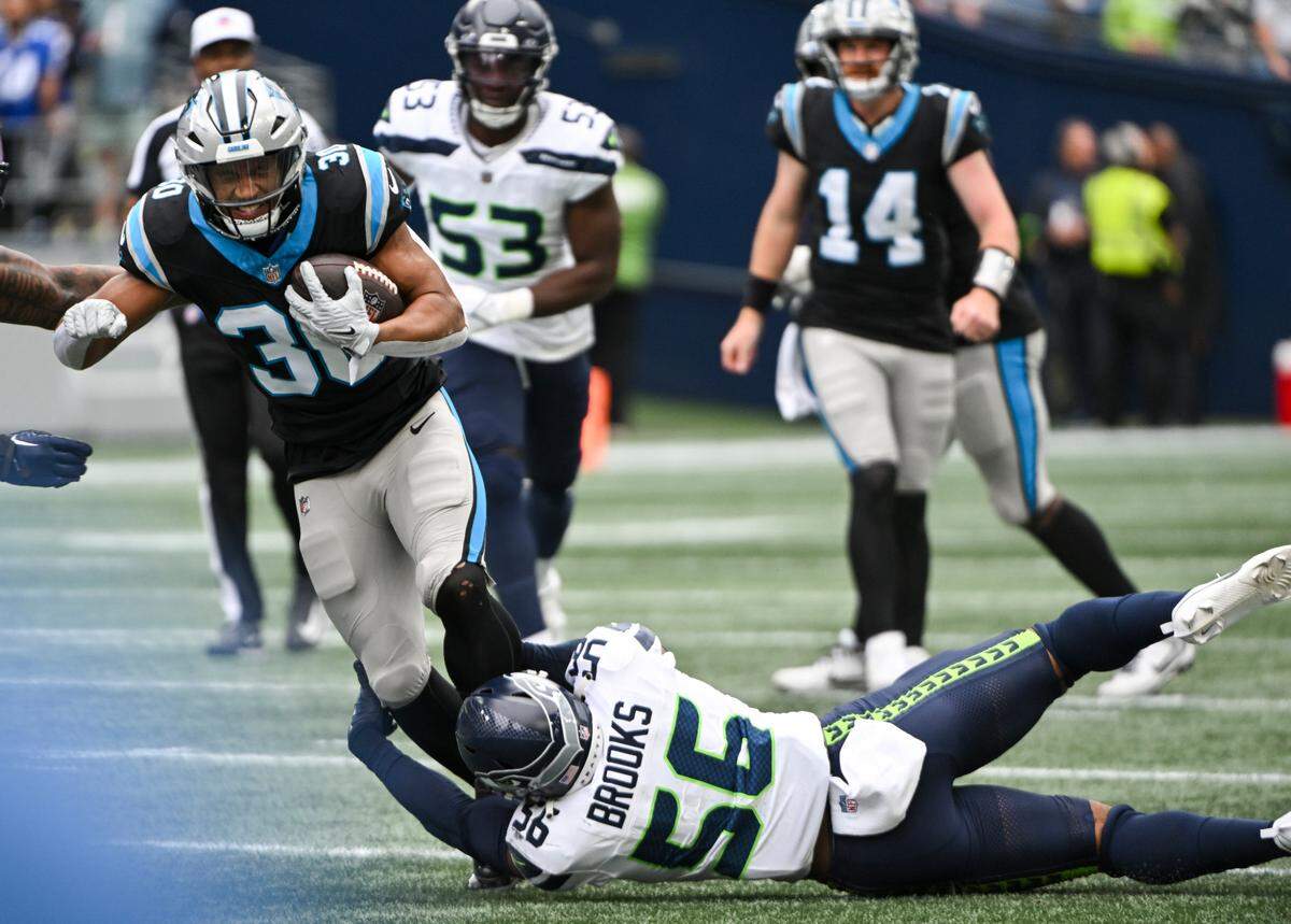 Carolina Panthers running back Chuba Hubbard (30) is tripped up by Seattle Seahawks linebacker Jordyn Brooks (56) during the second quarter of the game at Lumen Field, Sunday, Sept. 24, 2023, Seattle, Wash.