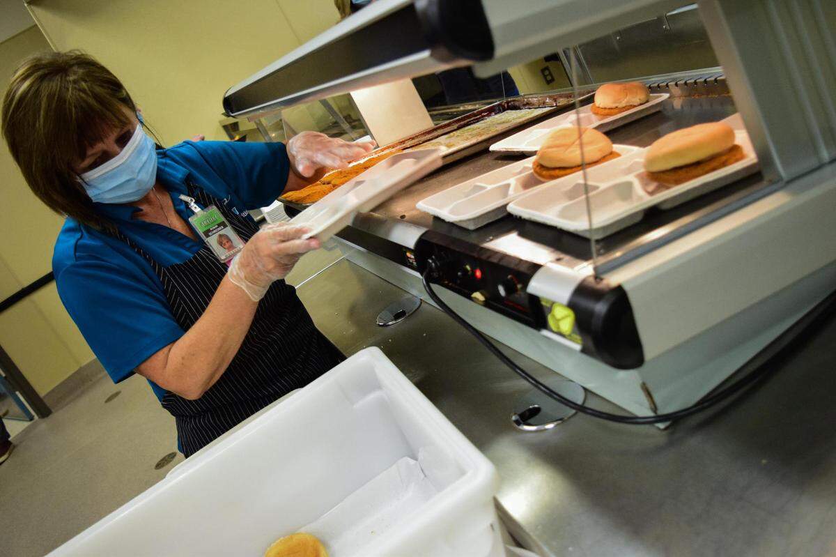 At Spanaway High School outside Tacoma, Wash., nutrition services employee Robin Schreiner prepares trays with chicken patty sandwiches on Oct. 20, 2021. Typically the school offers around six entrée choices, but pandemic supply issues have limited the number at most three.