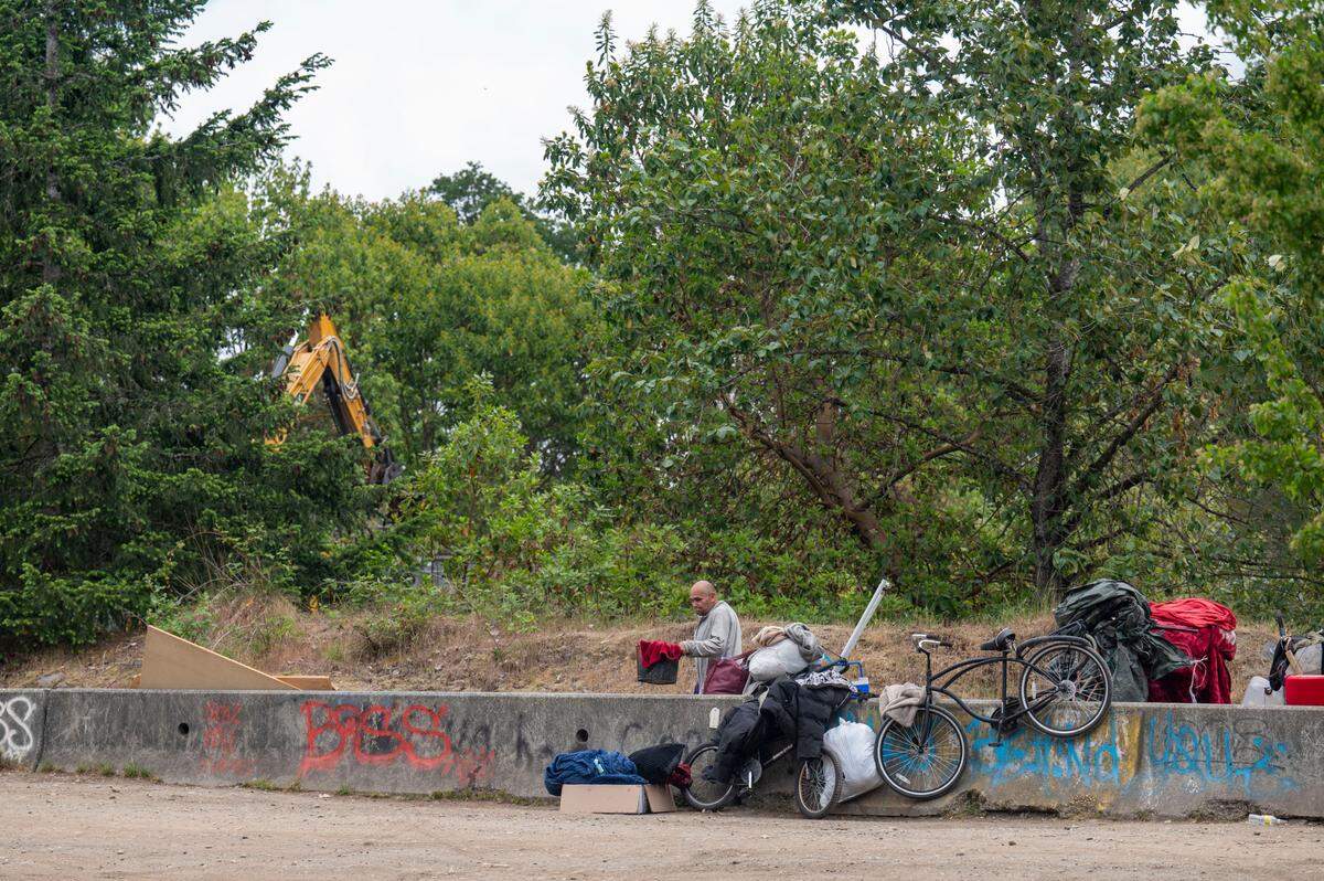A backhoe cleans up debris while a man gathers his belongings as a homeless encampment along South Tyler Street is cleared on Tuesday, May 30, 2023, in Tacoma, Wash.