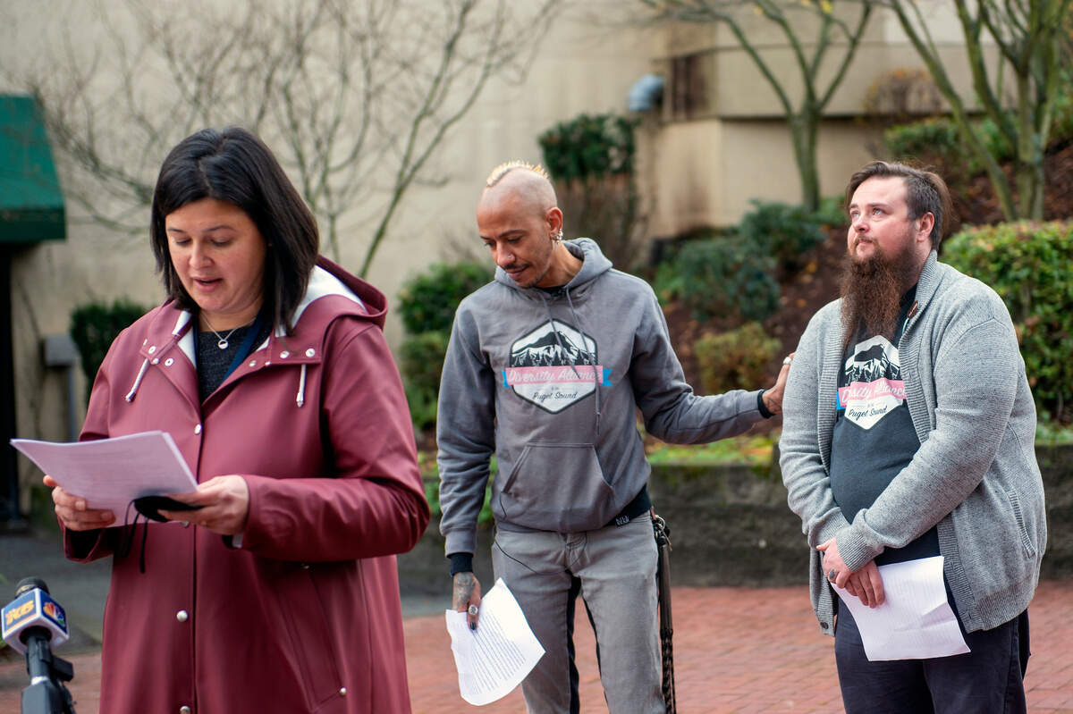 Tacoma City Council member Kristina Walker speaks, while Astro Pittman (center), board member at large for the Diversity Alliance of the Puget Sound, comforts Oliver Webb, the board chair of the same alliance group, after Webb spoke about the recent spike in violence toward transgender people during a Transgender Flag raising ceremony on Friday in downtown Tacoma.