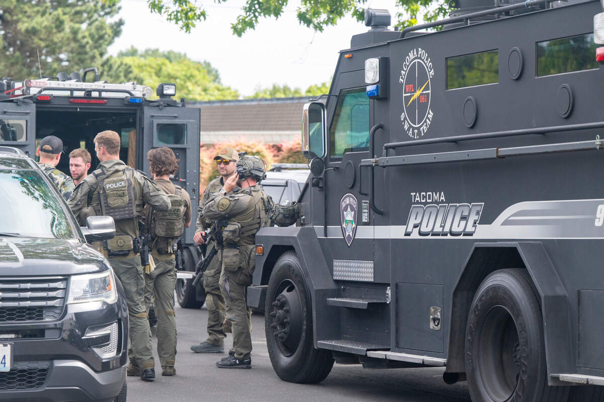 Tacoma police officers stand in a group between vehicles, including a SWAT vehicle, in the parking lot of The Church of Jesus Christ of Latter-day Saints along South 12th and South Pearl streets on Thursday, June 12, 2025, in Tacoma, Wash. More than a dozen police vehicles sat parked in the church lot after police officers were seen staging for an arrest operation in the area.