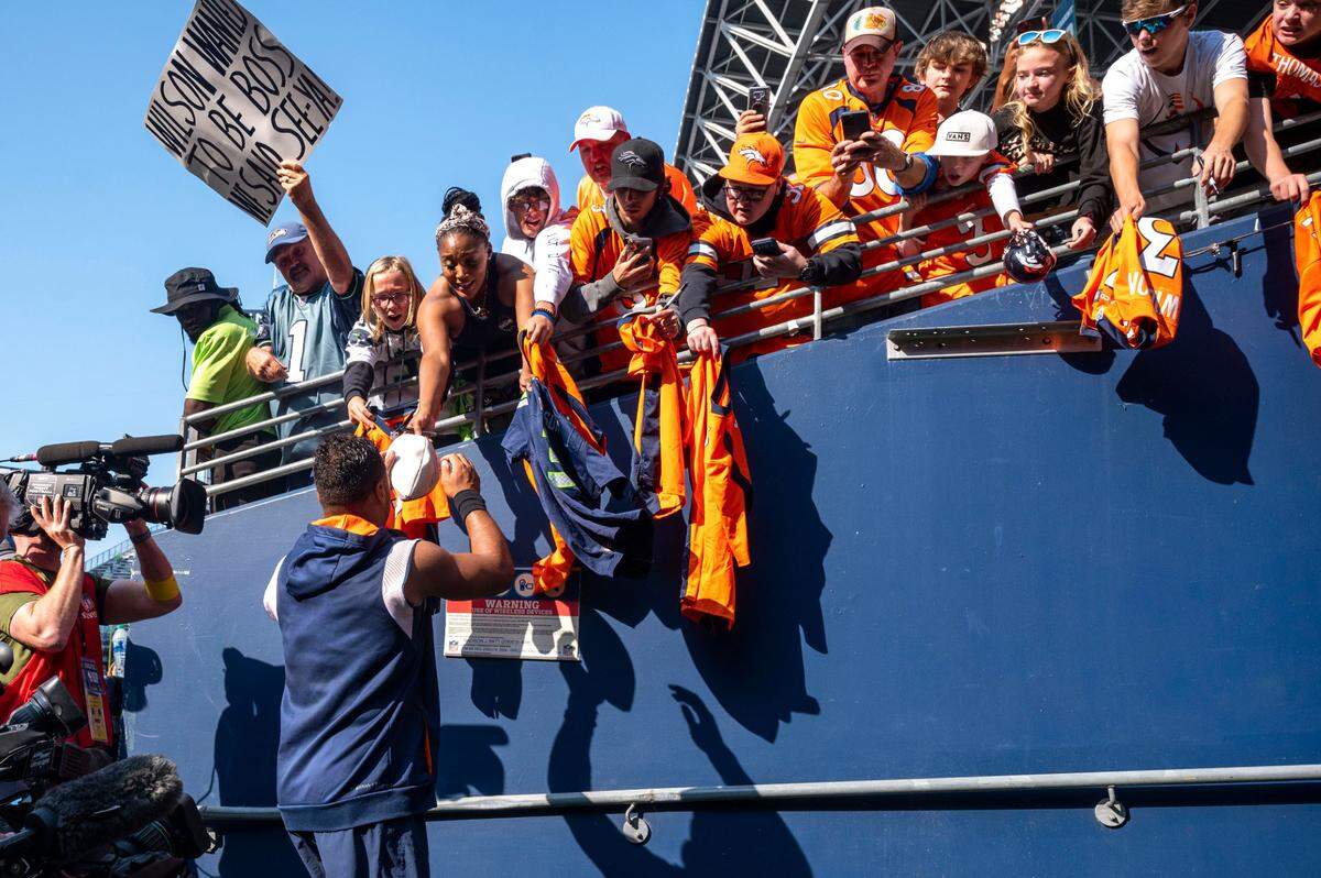 A Seattle Seahawk fan holds up a sign criticizing Denver Broncos quarterback Russell Wilson (3) as Wilson signs autographs for fans prior to an NFL game on Monday, Sept. 12, 2022, at Lumen Field in Seattle.