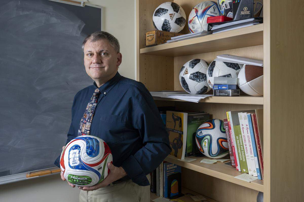 Professor John Eric Goff holds the Trionda ball, which will be used in next year’s FIFA World Cup, as he stands for a portrait in his office on Wednesday, Oct. 29, 2025, at the University of Puget Sound in Tacoma, Wash. Previous World Cup balls involved in his aerodynamics research sit on shelves nearby.