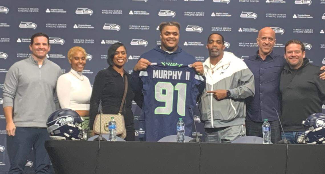 First-round NFL draft choice Byron Murphy II from the University of Texas holding his new Seahawks jersey flanked by his parents Byron Sr. and Seneca (immediately at his side), his girlfriend Maya Hurd (second from left), his agent Ron Slavin (second from right), coach Mike Macdonald (far left) and general manager John Schneider (far right).