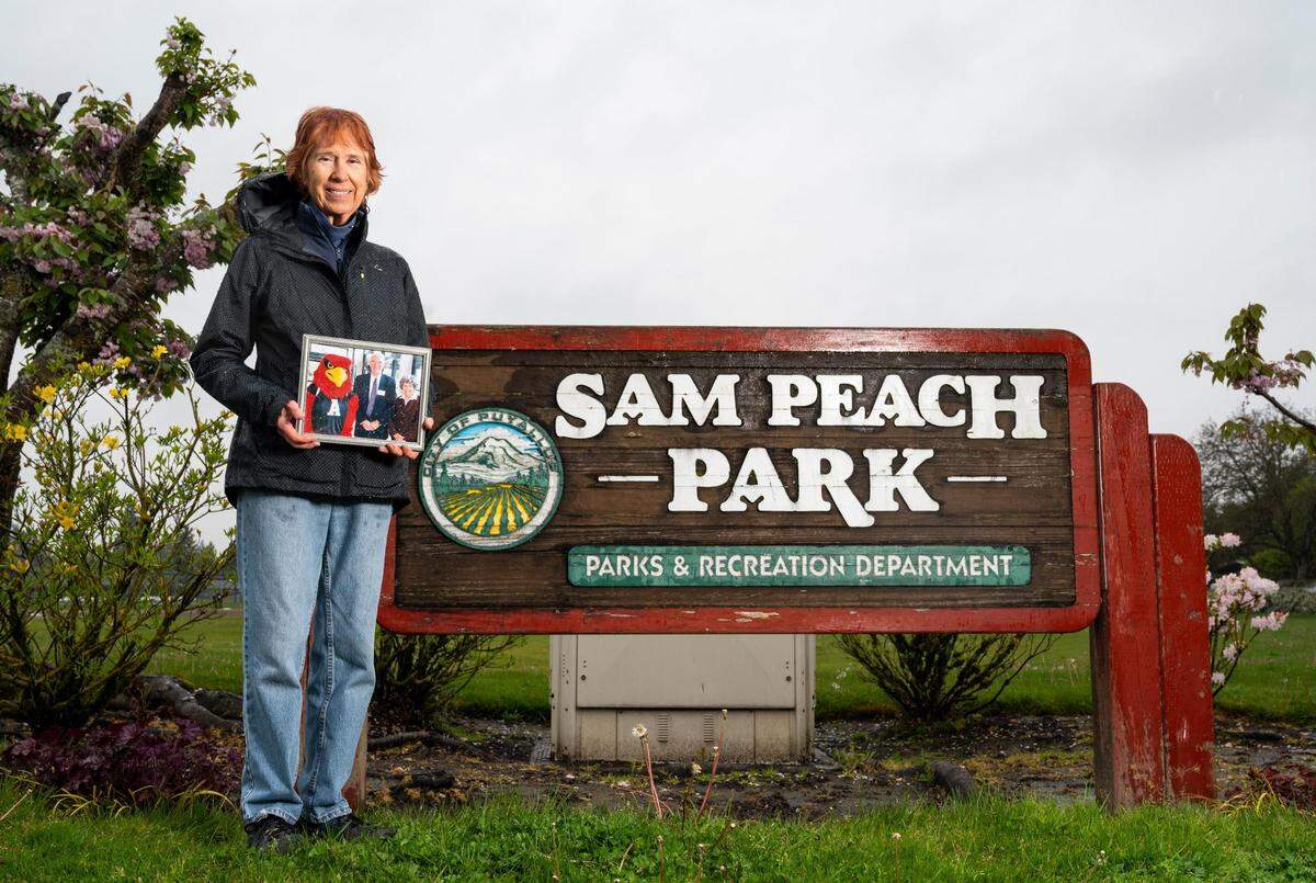 Kathi Peach-Cassidy, daughter of Sam Peach, a former Puyallup mayor who passed away in February at the age of 94, poses for a portrait with a photograph of her father at Sam Peach Park in Puyallup, Wash. on Thursday, May 5, 2022.