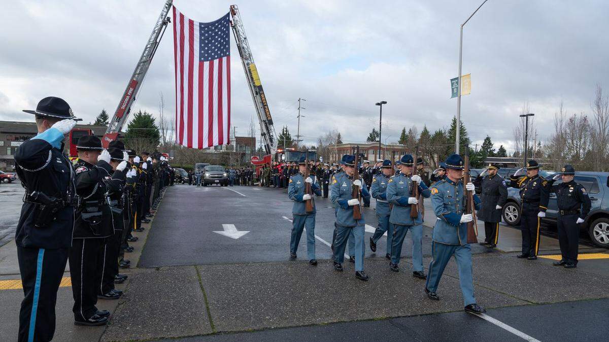 Washington State Patrol troopers march beneath a suspended American flag during the memorial service for Trooper Tara-Marysa Guting, who was killed in the line of duty while investigating a crash on SR-509.