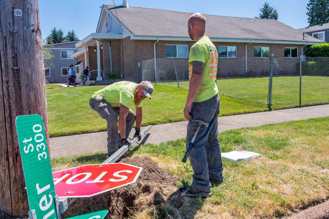 Construction workers from Global Contractors put up a street sign on the corner of South 54th Street and Warner Street as people walk into the House of Prayer Christian Church on Friday, June 24, 2022, in Tacoma. On Thursday, the church — and it’s affiliates in Texas and Georgia — was raided by the Federal Bureau of Investigation.