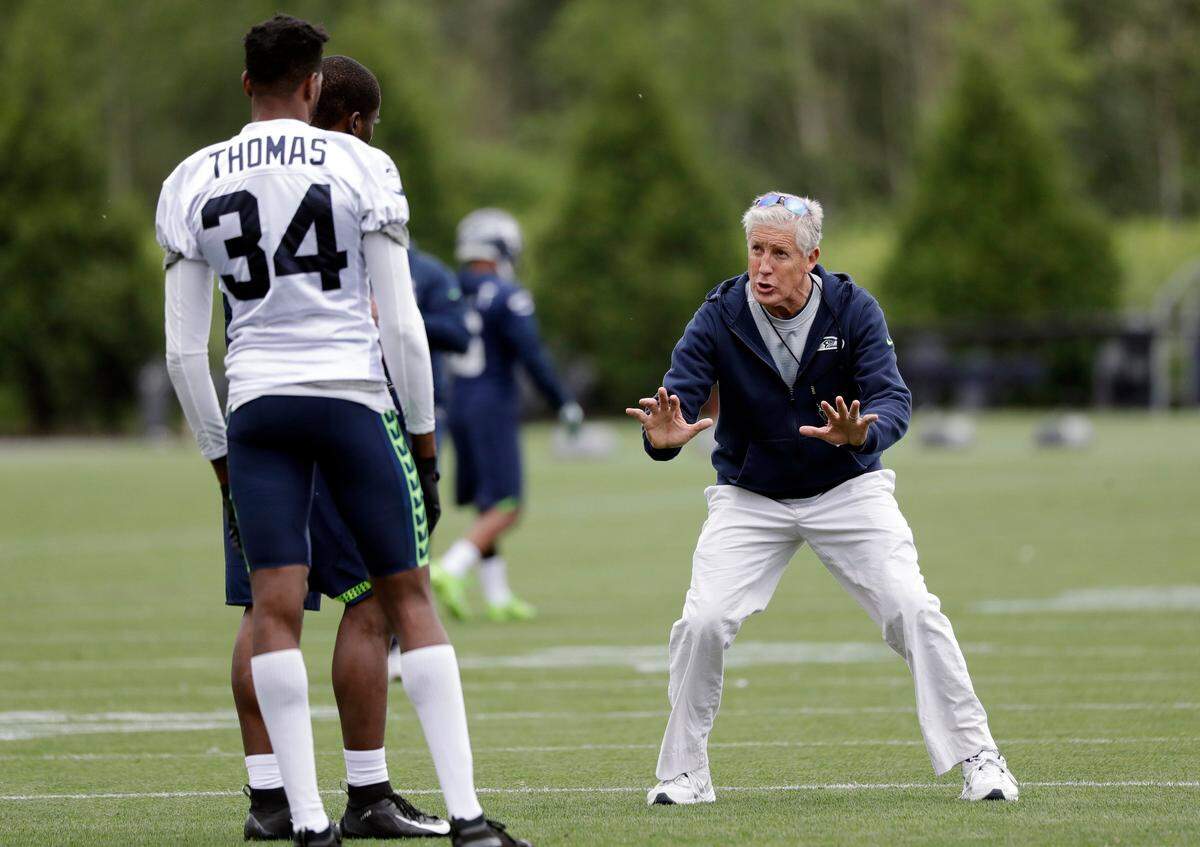 Coach Pete Carroll, right, works with defensive backs Simeon Thomas (34) and Davonte Davis after practice at Seahawks organized team activities on Tuesday in Renton.