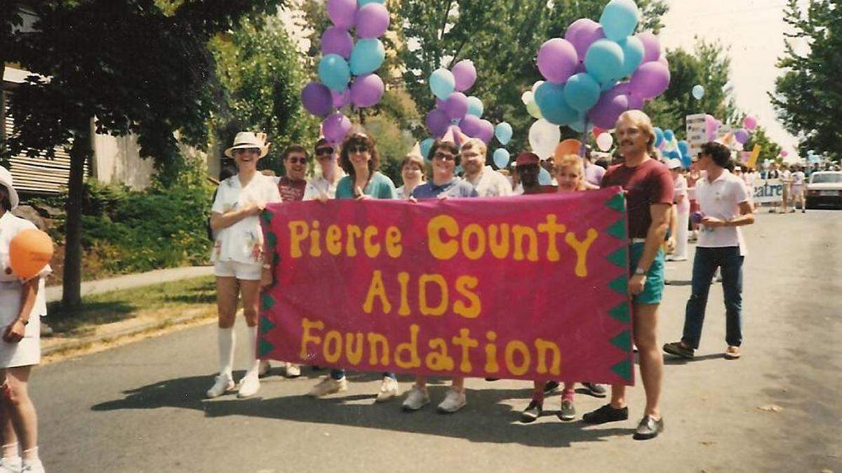 An archive photo from the early 1990s shows Pierce County Aids Foundation staff and community members at a Pride parade.