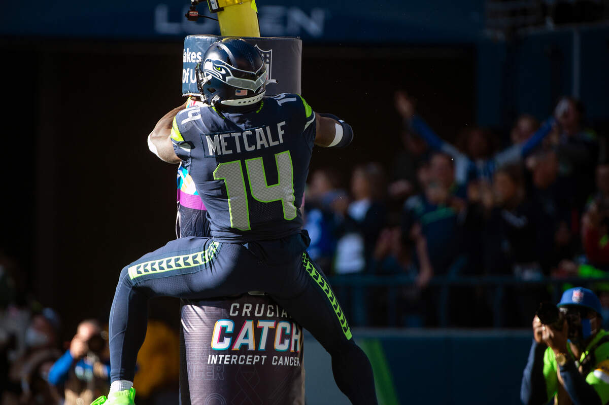 After catching a touchdown pass from quarterback Geno Smith (7), Seattle Seahawks wide receiver DK Metcalf (14) celebrates by jumping and hanging onto the base of the goal posts during the second quarter of an NFL game on Sunday at Lumen Field in Seattle. Metcalf was penalized for the celebration.