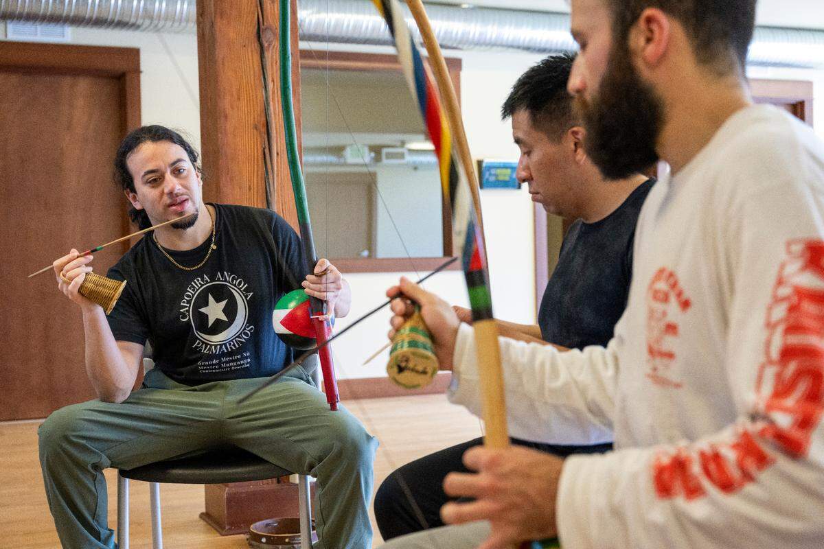 Instructor True “De Verdade” Emeka, left, gives pointers on the use of the Berimbau to students Israel Alvarez, center, and Anthony Asher as they play the instrument and sing along to traditional songs in a Capoeira class, or the Afro-Brazilian art form of martial art and dance, on Friday, April 18, 2025, at the Tacoma Capoeira Center in Tacoma, Wash.
