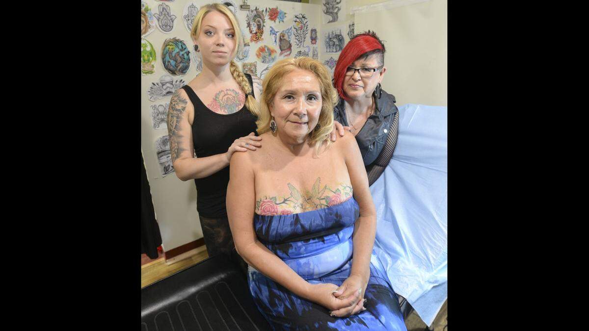 Tattoo artist Shelly James, left, Raynell Morris and Morris’ sister Raydean Finkbonner show off Morris’ tattoo that covers scars from her double mastectomy at Chameleon Ink in Bellingham in 2016. The design depicts two hummingbirds holding a pink ribbon.