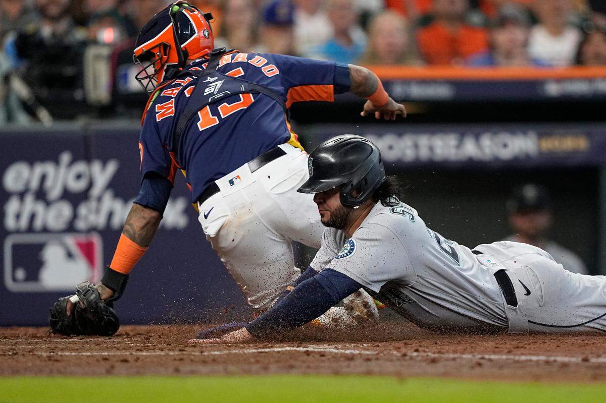 Seattle Mariners third baseman Eugenio Suarez, right, scores as Houston Astros catcher Martin Maldonado (15) missies the throw during the fourth inning in Game 2 of an American League Division Series baseball game in Houston, Thursday, Oct. 13, 2022. (AP Photo/David J. Phillip)