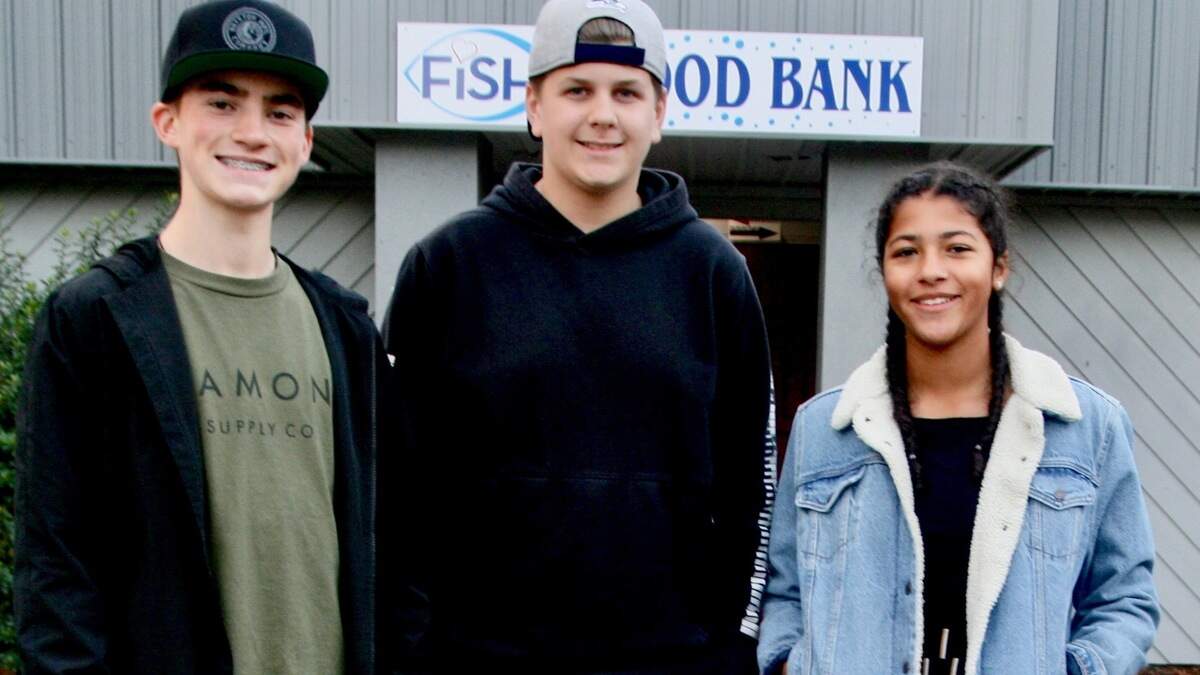 From left, Peninsula High School freshmen Jaiden Leach, Neiko Zanuttini and Donae Rumph pose before the Gig Harbor FISH Food Bank before delivering the proceeds of their food drive from Halloween night called “We Scare Hunger!”