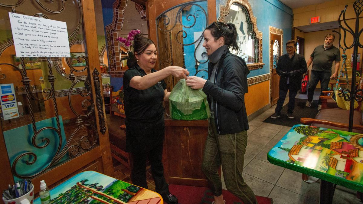 Gig Harbor resident Christina Manning has been “self-isolating” during the coronavirus crisis but she made an exception to pick up a takeout order at the “social distancing area” from Augustina Thomas at El Pueblito on Saturday, March 21, 2020. “This is my favorite restaurant and I want to support them,” said Manning, who also left a generous tip. As Gig Harbor restaurants struggle with the coronavirus closure, many are offering take-out, curbside pickup or home delivery.