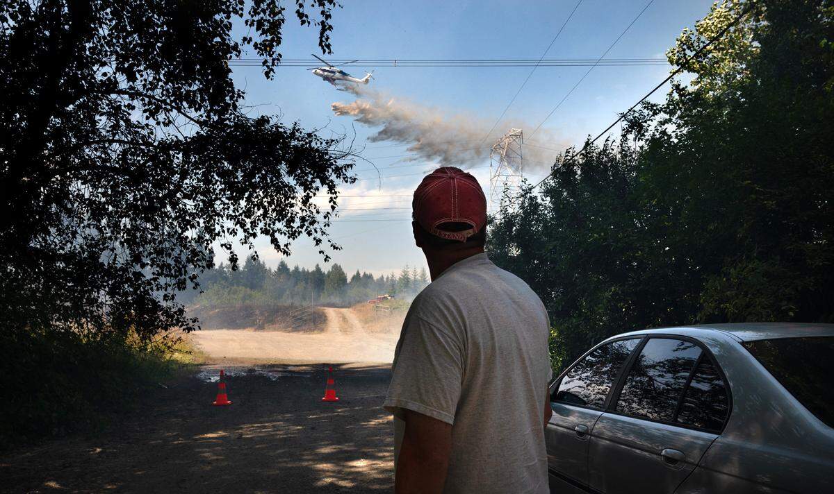 Neighbor Ken Linke watches as a helicopter drops water at a wildfire beneath the high tension power lines along 82nd Avenue South in Roy, Washington, on Thursday, July 6, 2023.