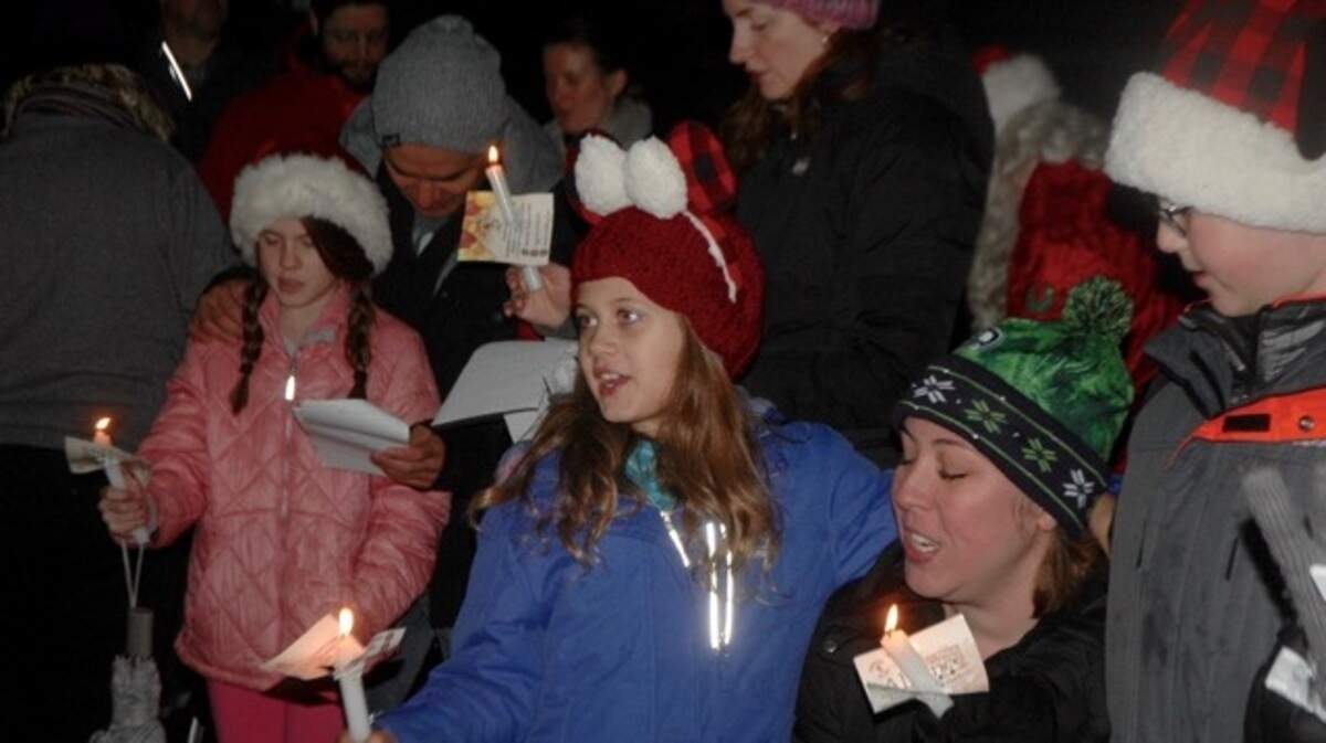 Ellie Hoskinson, 7, center, with mother Amy and, at far right, brother Matthew, 9, join in a carol at the traditional “Hark the Harbor” singalong in Skansie Brothers Park on Sunday. More photos below.