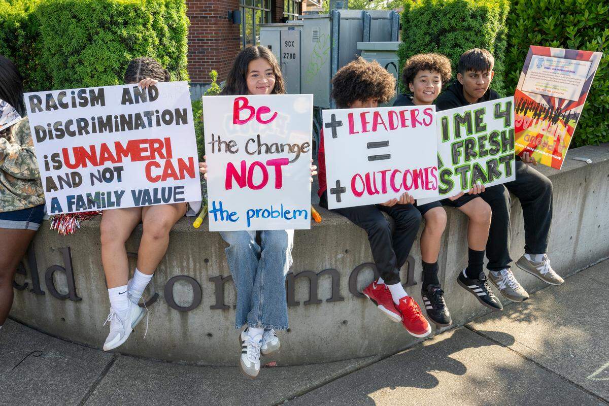 A group of students from the Franklin Pierce School District, including, from left, Viviana, Boston Chang, AJ, Eli Chang and Elmer Umana, sit with signs at the intersection of Garfield Street South and Pacific Avenue South with a group gathered to call attention to issues like discrimination and budgetary cuts in the district. Photographed on Tuesday, June 3, 2025, in Pierce County.
