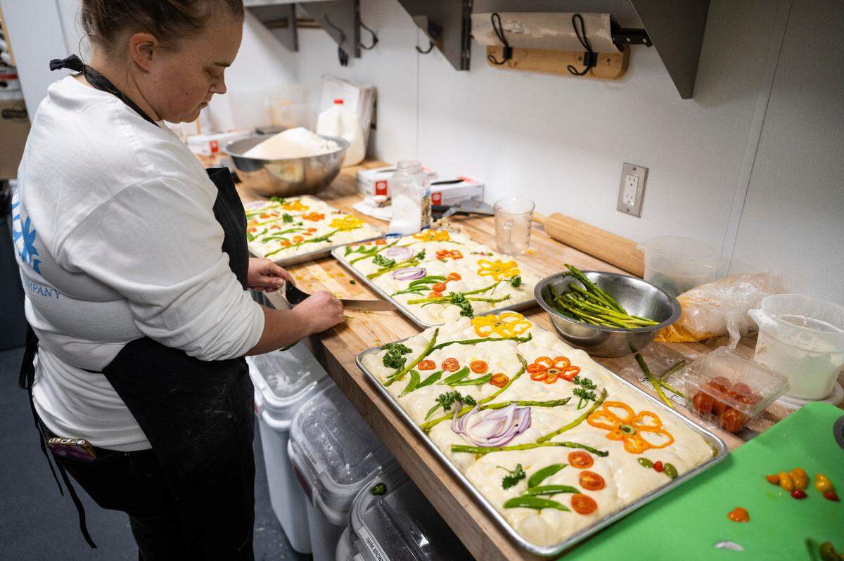 Farm 12 baker Abby Heath decorates the house focaccia with jalapeños, onions, asparagus and peppers on Wednesday, Nov. 2, 2022. You can buy focaccia, loaves of sourdough and brioche at fika.