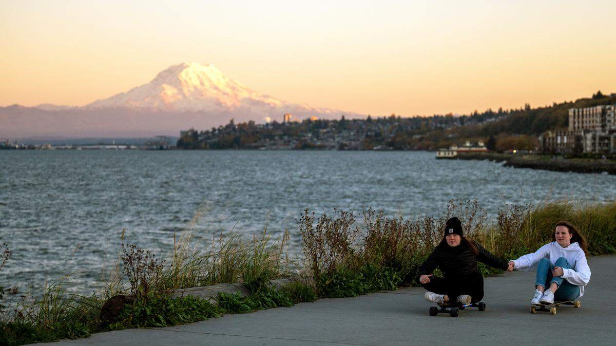 Mount Rainier glows in the sunset as a pair of skateboarders ride along the walking path at Ruston Point near Dune Park on Saturday evening.